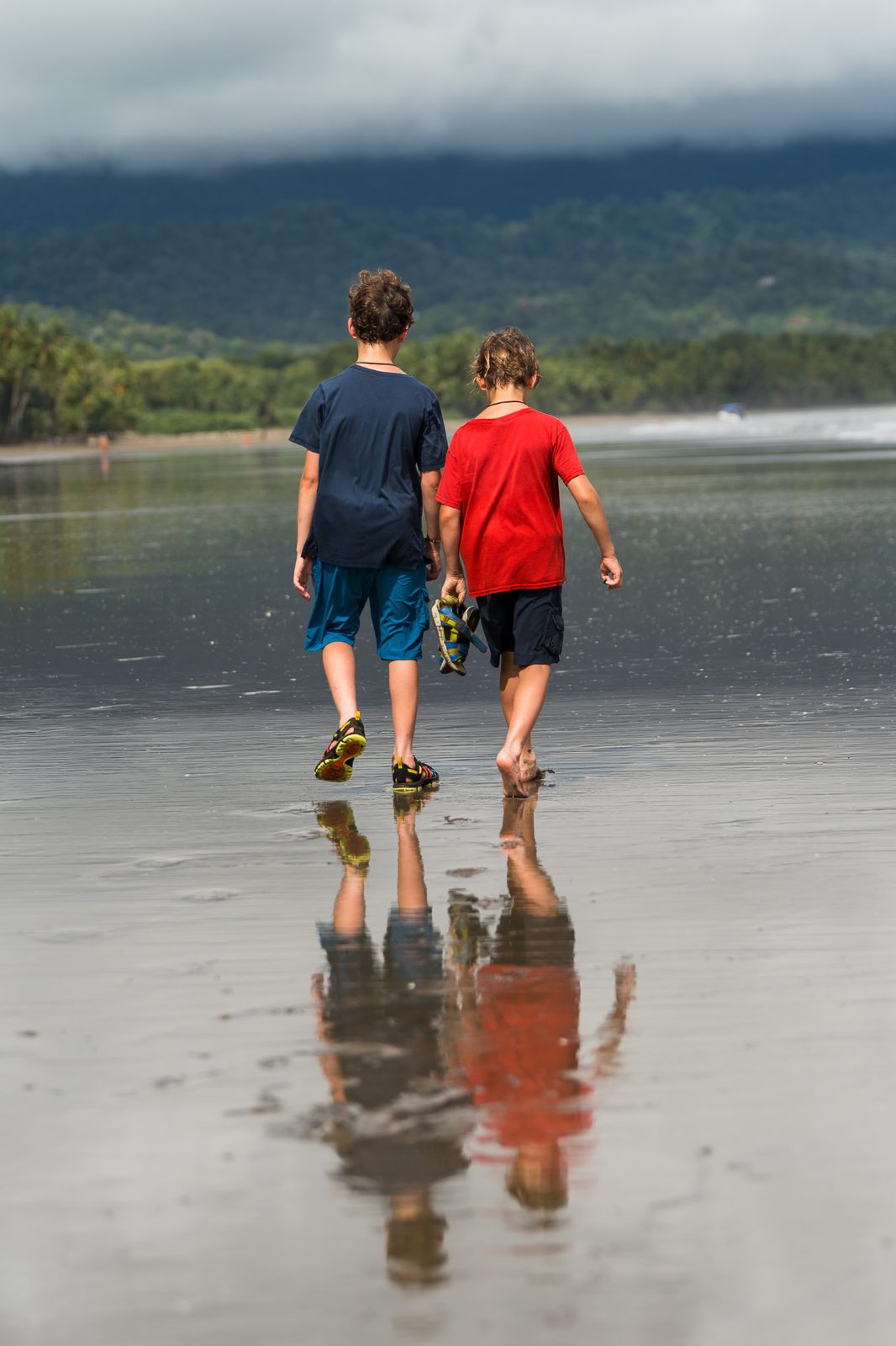 Two boys walking away across a wet beach, reflected in the sand